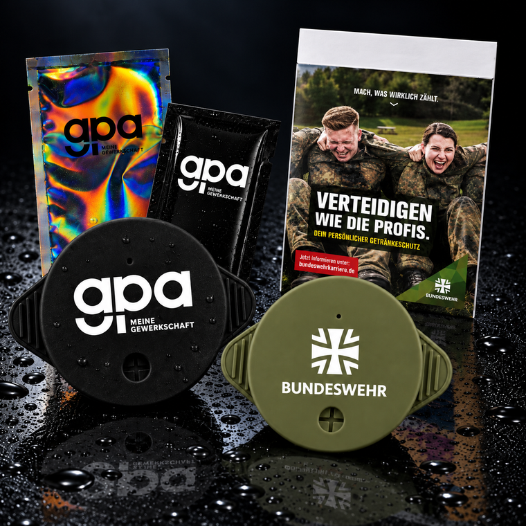 Schwarzer GPA-Silikondeckel und olivgrüner Bundeswehr-Silikondeckel mit flacher Papierverpackung auf dunklem Hintergrund.